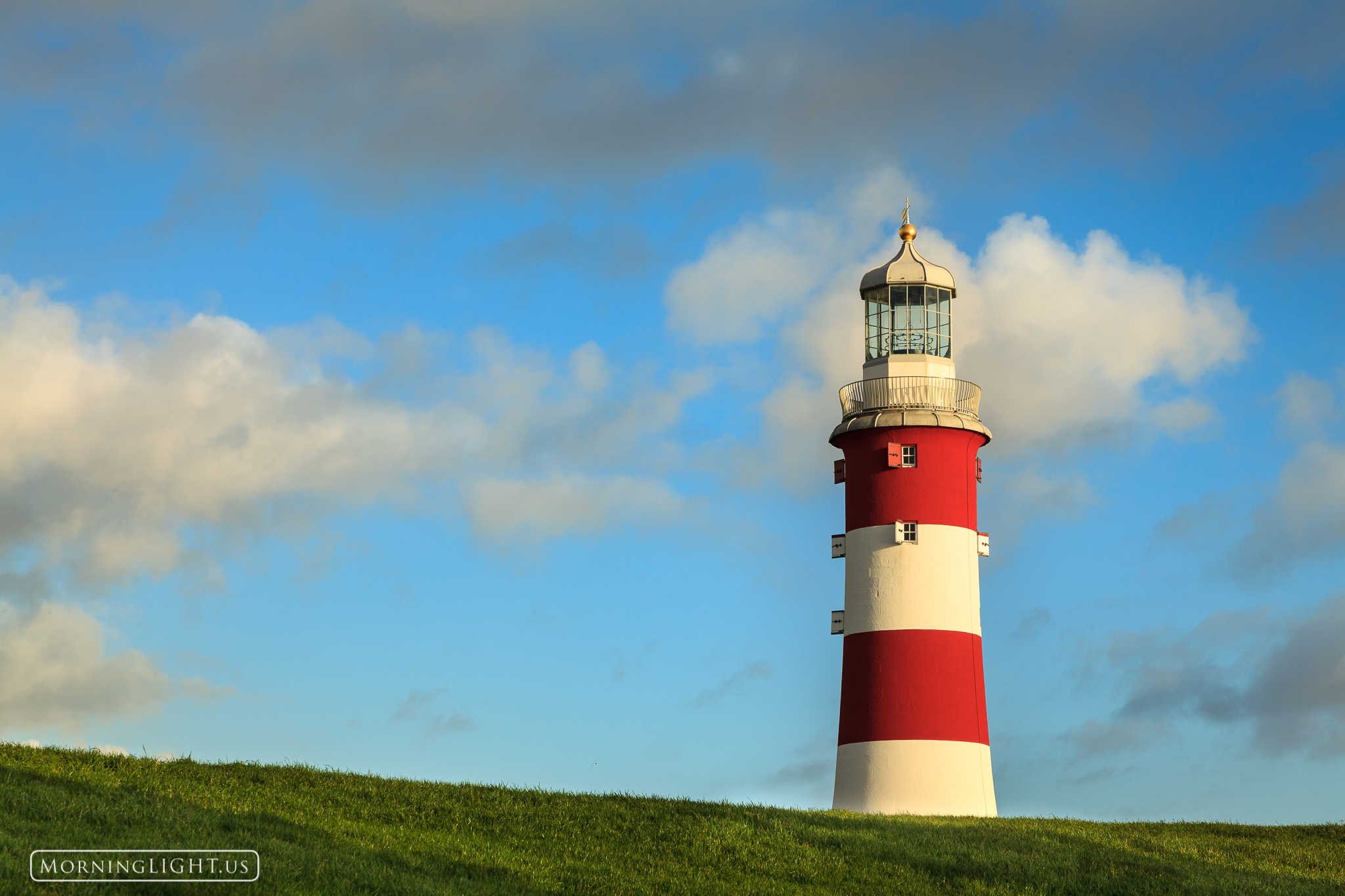 A red and white lighthouse stands above a grassy green field in Plymouth England.